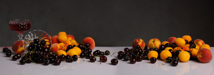 Panorama with cherries, peaches, apricots and a glass of wine on a dark background