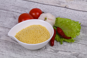 Raw couscous in the bowl served salad leaves, tomato and pepper