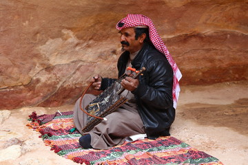 Fototapeta premium Petra, Jordan - May 22, 2019. A man in traditional costume plays music in Petra