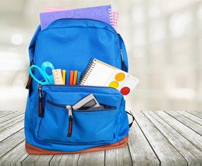 Open blue school backpack on wooden desk and gray background.
