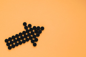 Medical activated carbon in the form of an arrow on a orange background. Top view, copy space.