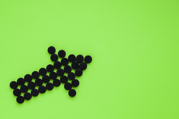 Medical activated carbon in the form of an arrow on a green background. Top view, copy space.