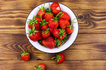 Fresh ripe strawberry in white bowl on a wooden table. Top view