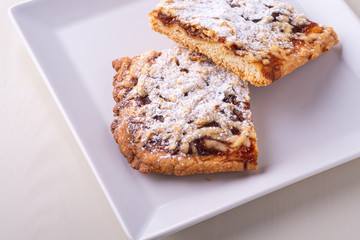 Two pieces of homemade cookies apricot jam powdered sugar in white square plate