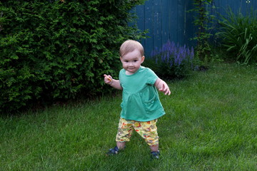 Horizontal full length view of cute fair toddler girl with cheeky expression learning to walk in lawn