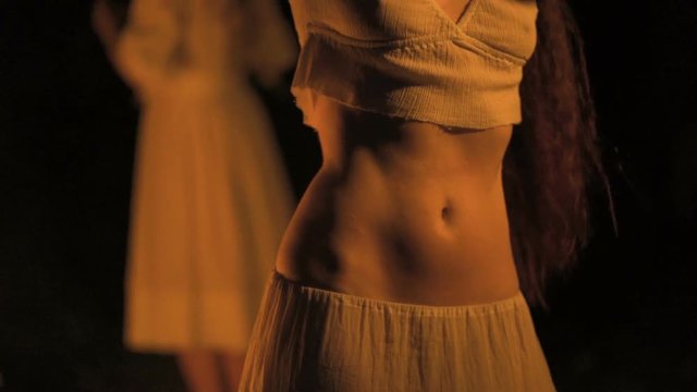 Curly brunette dancing belly dance near the fire, in the background sunset