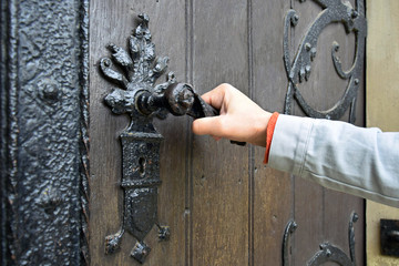 Man opens an ancient wooden door decorated with wrought iron elements. Old lock with an iron...