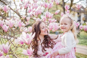 Fototapeta premium Beautiful young mother and little daughter near a blooming magnolia. Spring. Pink blooms.