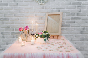 Large pink roses stand in glass vases along with candles in glass cups, on the table are homemade wooden hearts. Wedding ceremony. Scenery and details. Evening traditions.