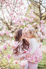 Fototapeta premium Beautiful young mother and little daughter near a blooming magnolia. Spring. Pink blooms.