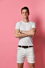 Fototapeta na wymiar Young smiling man in denim shorts and white t-shirt, isolated on pink