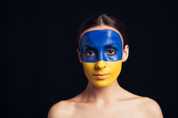 naked young woman with painted Ukrainian flag on skin looking at camera isolated on black