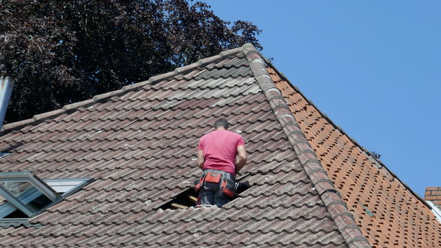 Hole in the roof of a residential building. Repair of a tile roof after a storm damage.