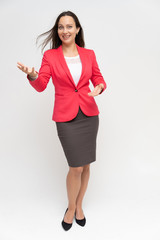 Full-length portrait of a young pretty brunette woman 30 years old in a bright red business suit with beautiful dark hair. Standing on a white background, talking, showing hands, with emotions