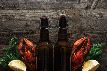 top view of red lobsters, dill, lemon slices and glass bottles with beer on wooden surface
