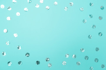 Frame of shiny silver confetti on pastel turquoise paper background. Concept of holiday, birthday, blogging, beauty. Top view. Flat lay. Minimal style mock up. Template for blog. Copy space