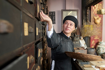 Fototapeta na wymiar Asian herbs store worker opening drawer to take out dry ingredients for recipe
