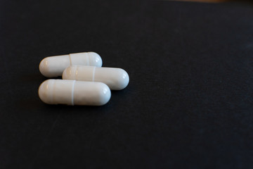 Fototapeta na wymiar 3 / three white pills, capsules isolated on dark / grey background