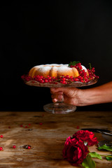 Bundt cake with currant and roses flowers on the black background.