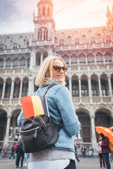 Naklejka premium Woman traveler with backpack and flag of Belgium stands on Grand Place Square in Brussels, Belgium