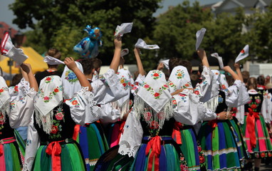 Polish women and girls in traditional colorful folk dresses from Lowicz region walk in street during Corpus christi holiday while waving handkerchief