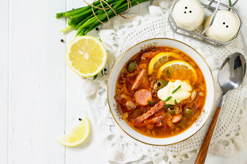 Traditional Russian soup Solyanka with meat, sausages, vegetables, capers, pickles and olives with lemon on wooden table. Rustic style. Top view flat lay background. Free space for your text.