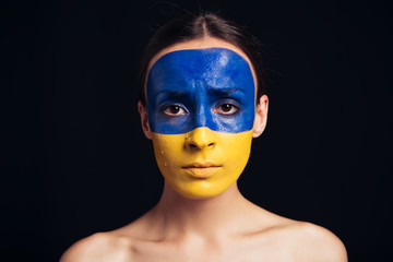 naked young woman with painted Ukrainian flag on face isolated on black