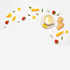 White cup of tea and fresh strawberries, pieces of ginger, orange, mint and sugar on a gray background. Flat lay, top view.