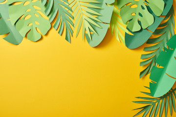 top view of paper cut green palm leaves on yellow background with copy space