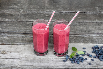 Two transparent glasses with plastic tubes with drinking smoothie from fresh wild honeysuckle and...