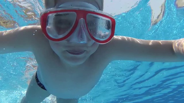 Closeup underwater portrait of cute funny white kid swimming in blue summer pool outdoor. Real time full hd video footage.