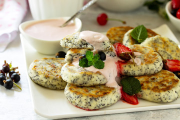 Summer breakfast background close-up. Homemade cottage cheese pancakes with poppy seeds, served sour cream sauce with strawberries.
