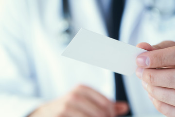 Male physician's hand holding and giving white blank calling card closeup in office. Contact information exchange, introducing gesture at formal meeting, personal or family doctor concept