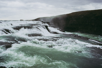 Cascade waterfall in Iceland. White splashes, turquoise water, and black rock under the gray sky. Spring