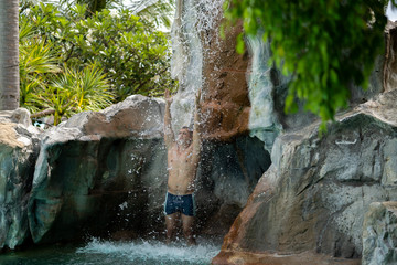 A young guy stands under artificial waterfalls in the pool on site