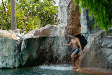 A young guy stands under artificial waterfalls in the pool on site