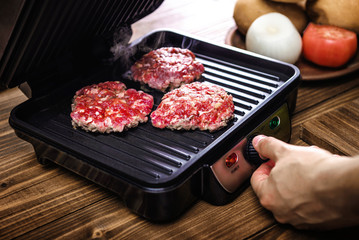 Grilling meat for hamburgers in an electric grill on a wooden table