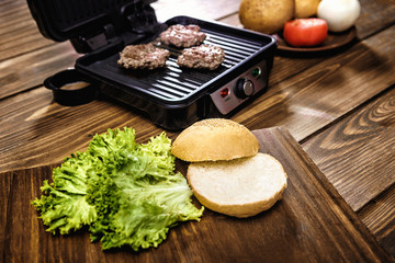 Cooking home burgers using electric grill on a wooden table