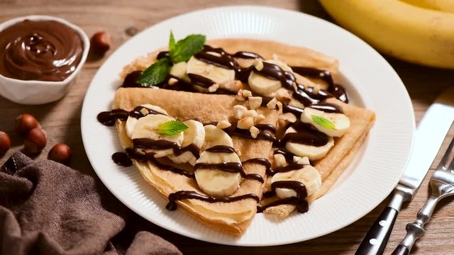 Rotating Banana Chocolate Crepes Served On White Plate, Wooden Table Background