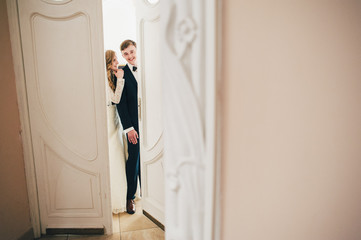 A stylish elegant bride with bouquet of wedding flowers hugging groom, stand, look and open the door. Close up. Portrait. Retro. Vintage architecture indoors. Exit through the door.