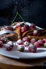 Fototapeta na wymiar Pancakes on a black background with juicy berries, condensed milk and powdered sugar. Pancakes on a white plate and wooden oak board. Food on a black background. Levitating Food, Levitating Berries
