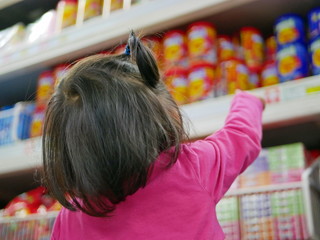 Little baby girl pointing at colorful snacks / candies on the shelves in a supermarket, wanting her...