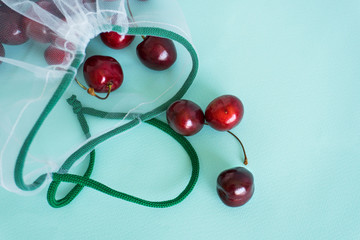 cherry in a reusable fabric transparent bag on a blue background in the fight against plastic. close-up corner composition
