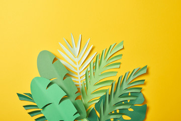 Fototapeta na wymiar bunch of paper cut exotic green palm leaves on yellow background with copy space