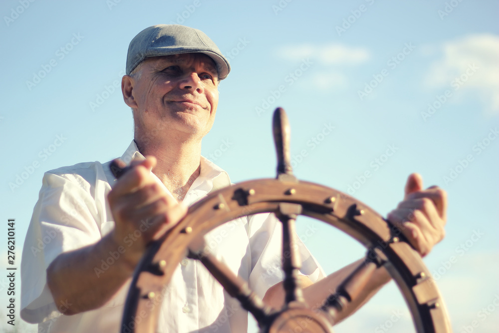 Wall mural a man controls the yacht, hands on the steering wheel, handwheel on sky background