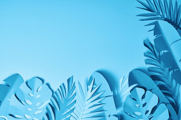 Fototapeta na wymiar top view of blue exotic paper cut palm leaves on blue background with copy space