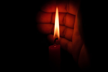 Hand protecting candle light from the wind in darkness on black background