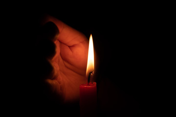 Hand protecting candle light from the wind