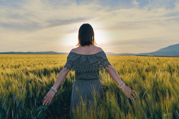 Young woman walks through wheat field in the summer at sunset - golden hour