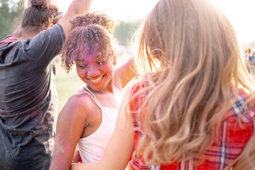African American young woman covered in colorful powder with friends at holi festival